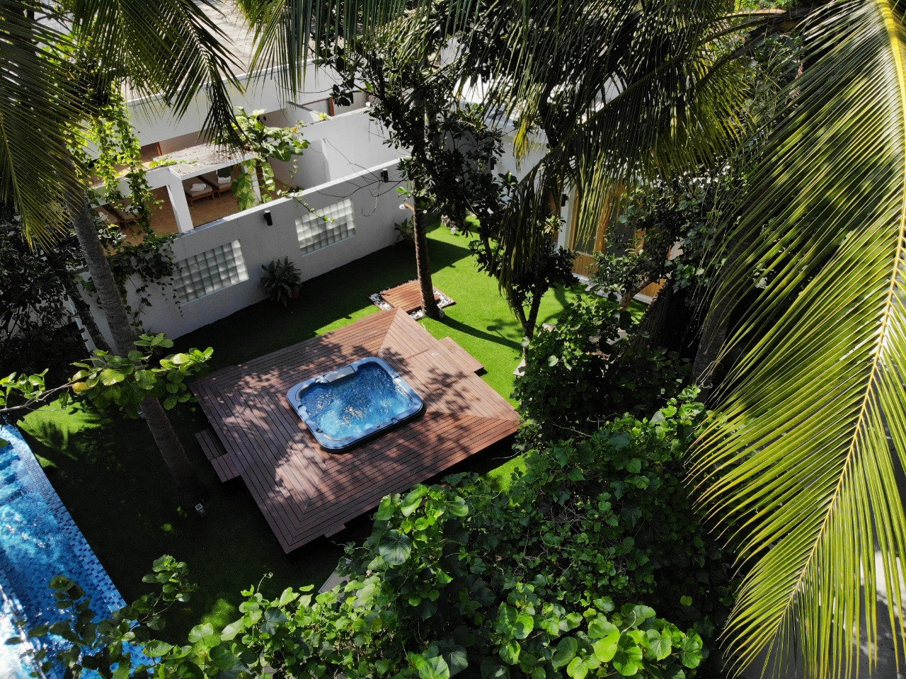 A sunken jacuzzi set into a timber deck, surrounded by palms and dense tropical greenery beside a villa pool.